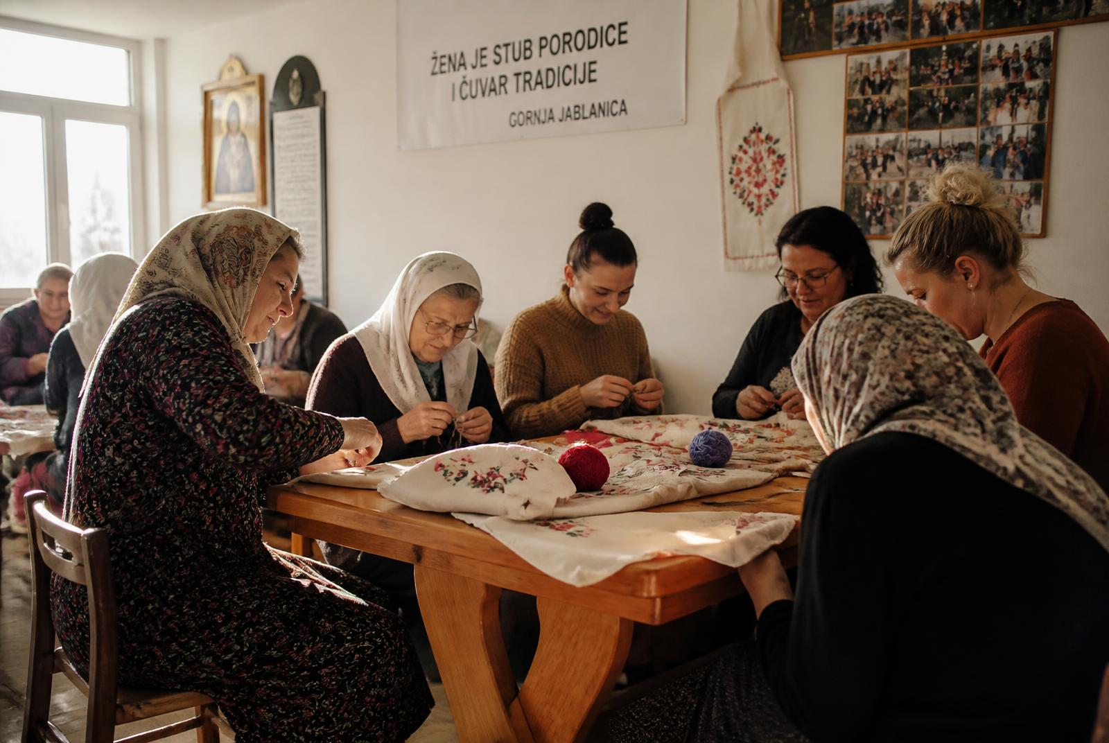 Women of different generations embroidering together in a community hall in central Bosnia